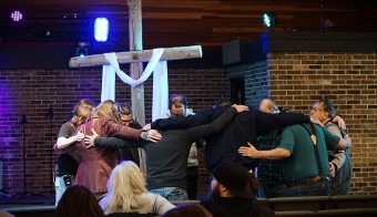 a group of people in a circle praying with arms around each other
