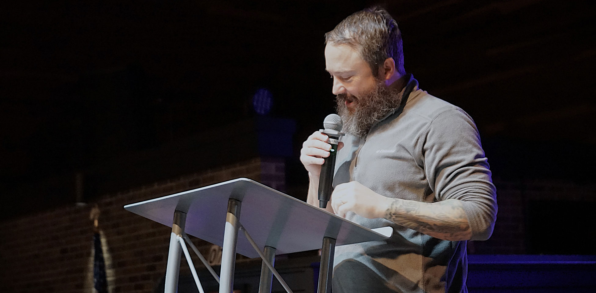 Brandon Wright, a beardy man with tattoos, preaching at a pulpit